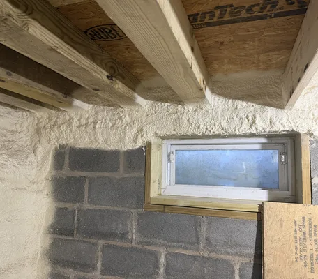 Closed-cell spray foam sealing rim joists and band boards around a basement window in a new build